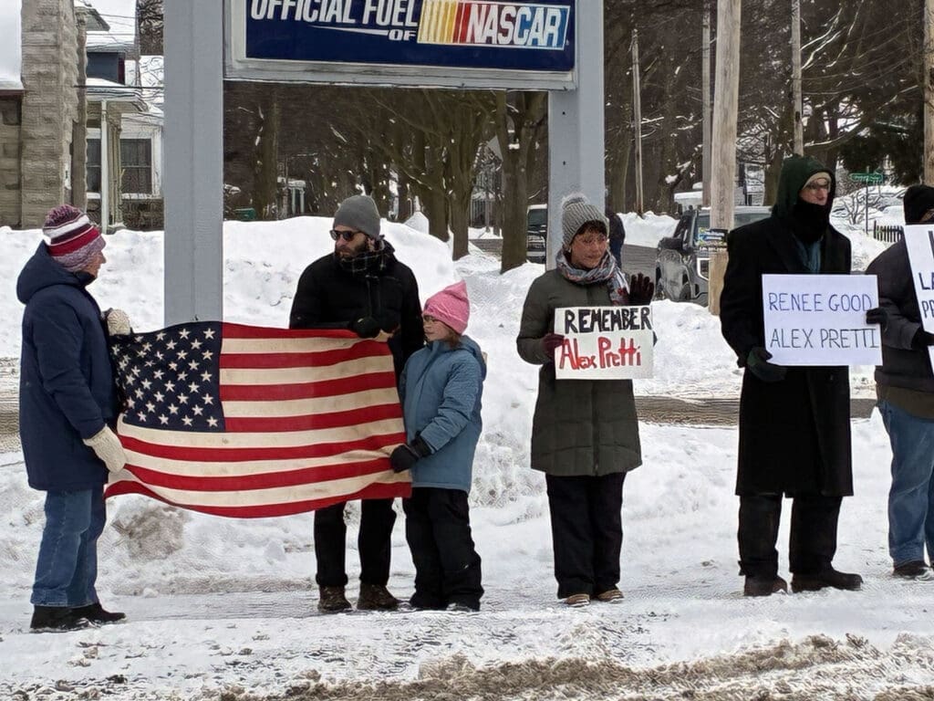 People hold American flag and signs in snowy protest.