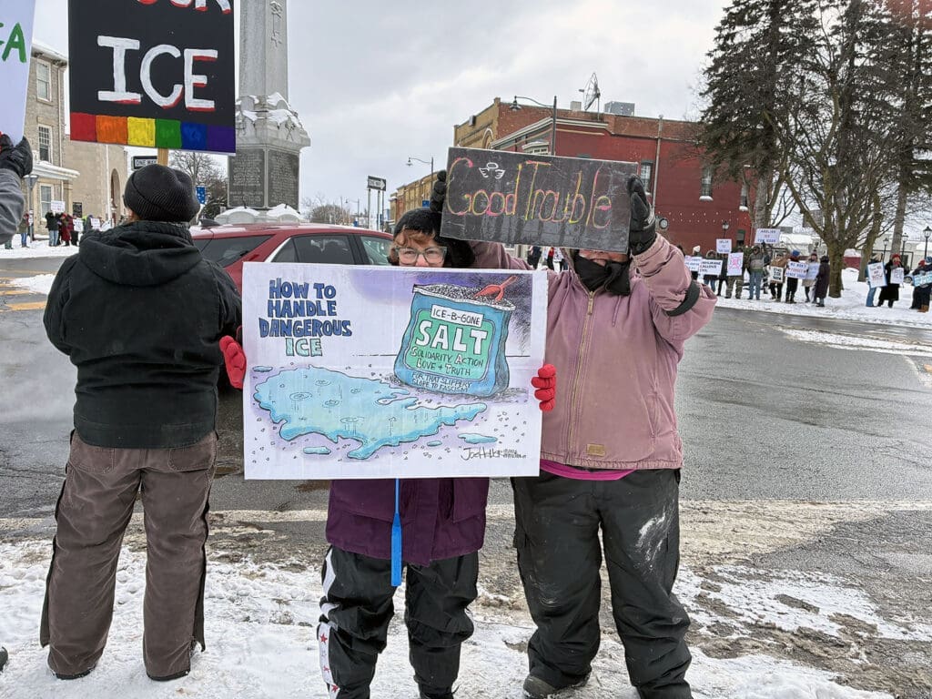 Protesters with signs on snowy street corner.