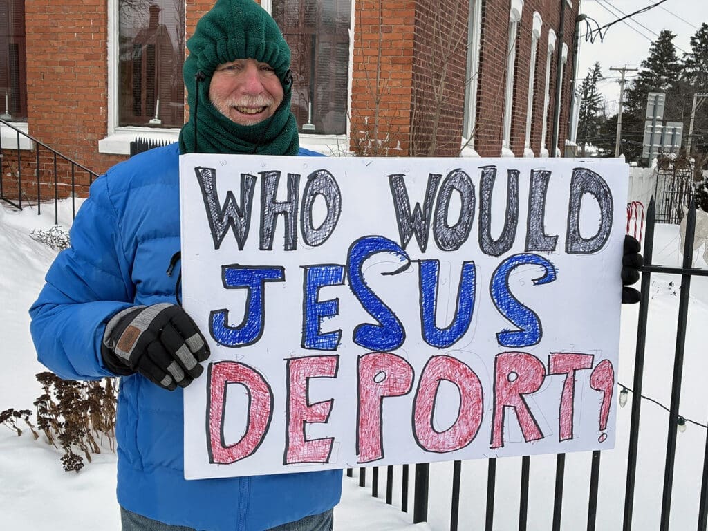 Person holding sign: Who Would Jesus Deport?