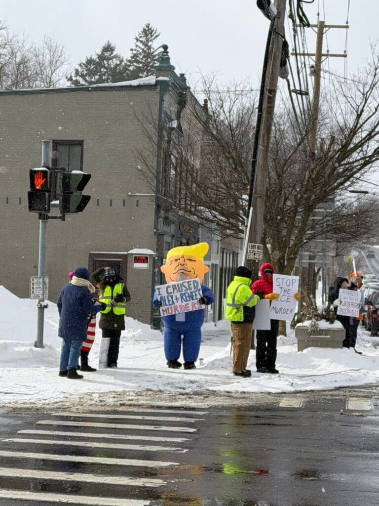 Protesters hold signs on snowy street corner.