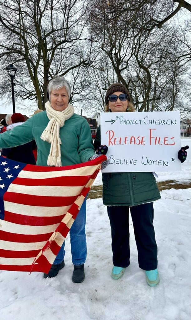 Women protest with signs and American flag in snow.