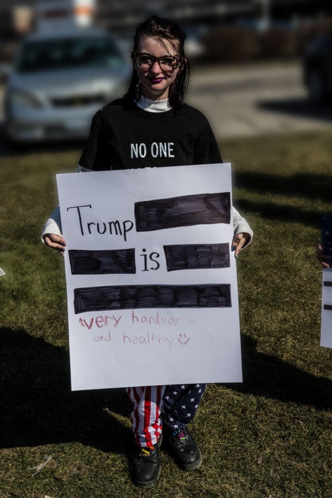 Woman holding anti-Trump protest sign at outdoor rally