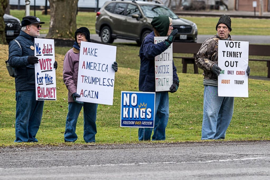 Protesters holding anti-Trump political signs outdoors.