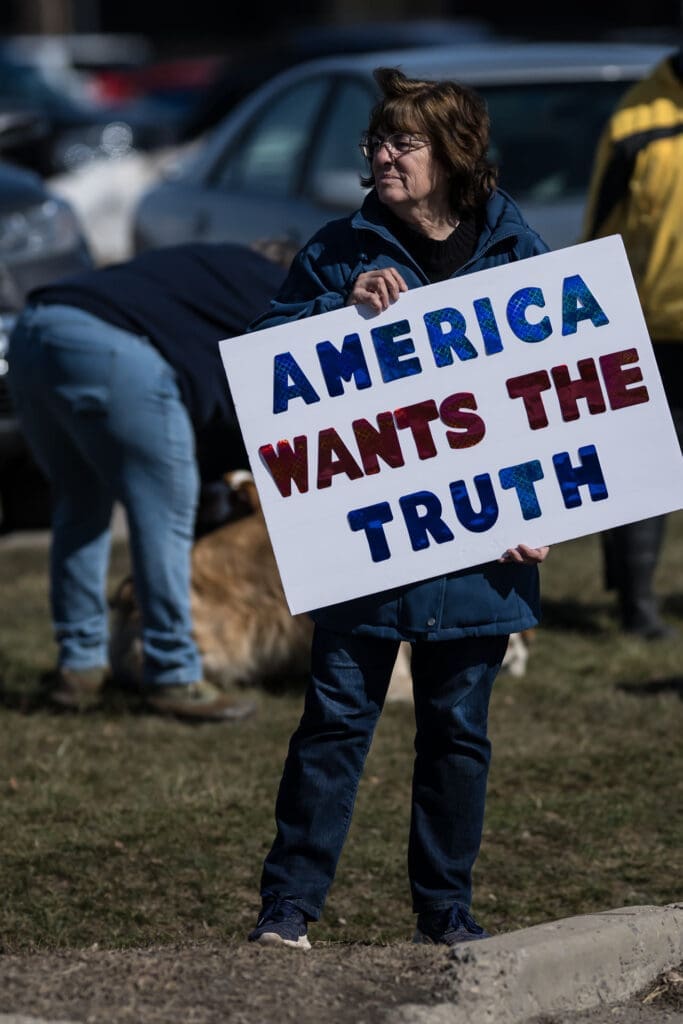 Woman holding 'America Wants The Truth' protest sign