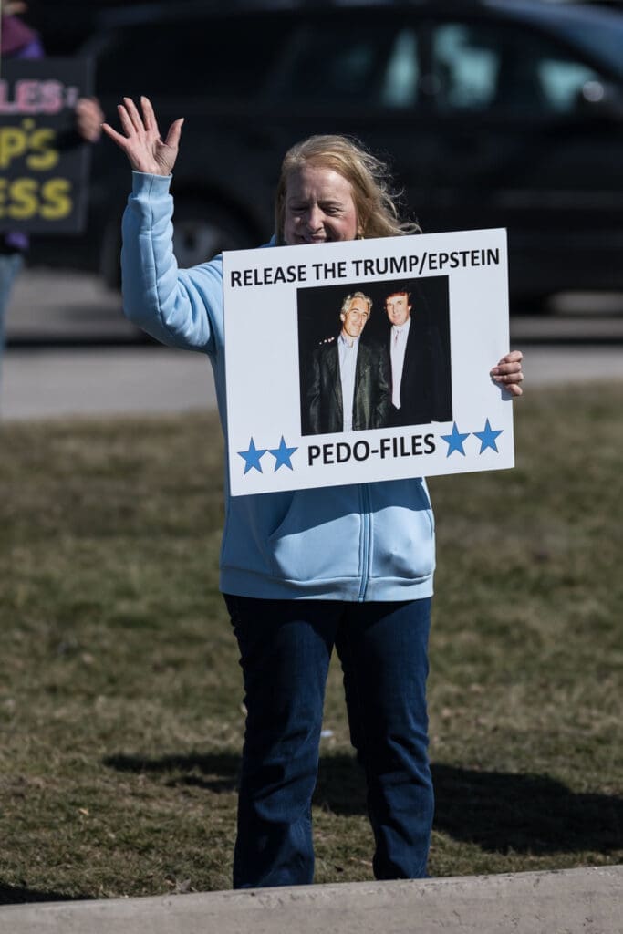 Woman holding protest sign about Trump-Epstein files