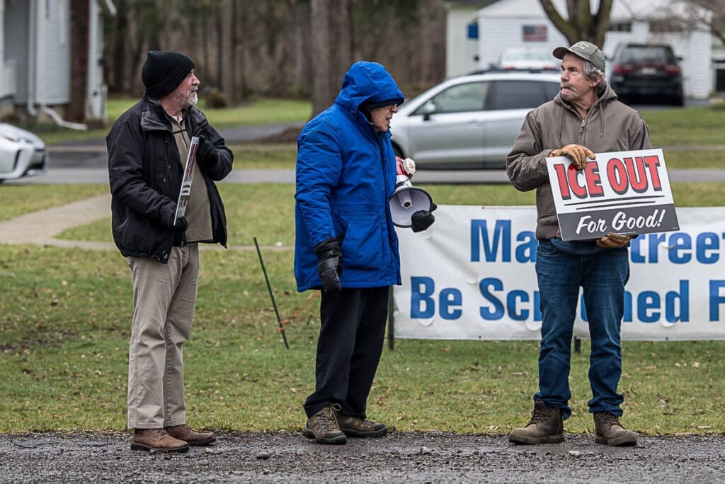 Men protesting outdoors holding ICE Out sign
