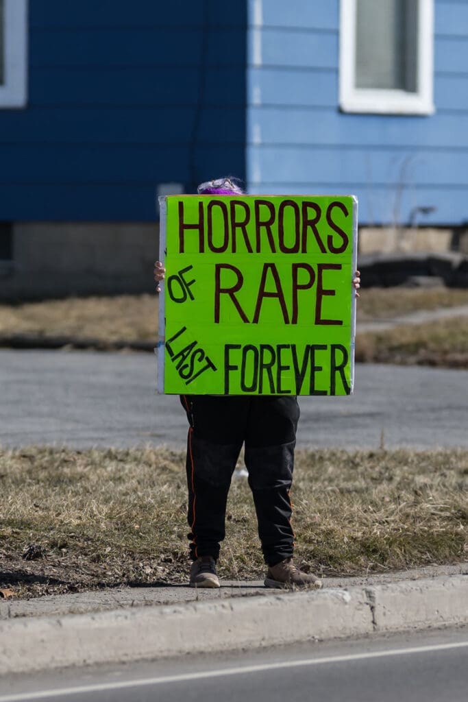 Person holding green protest sign about rape