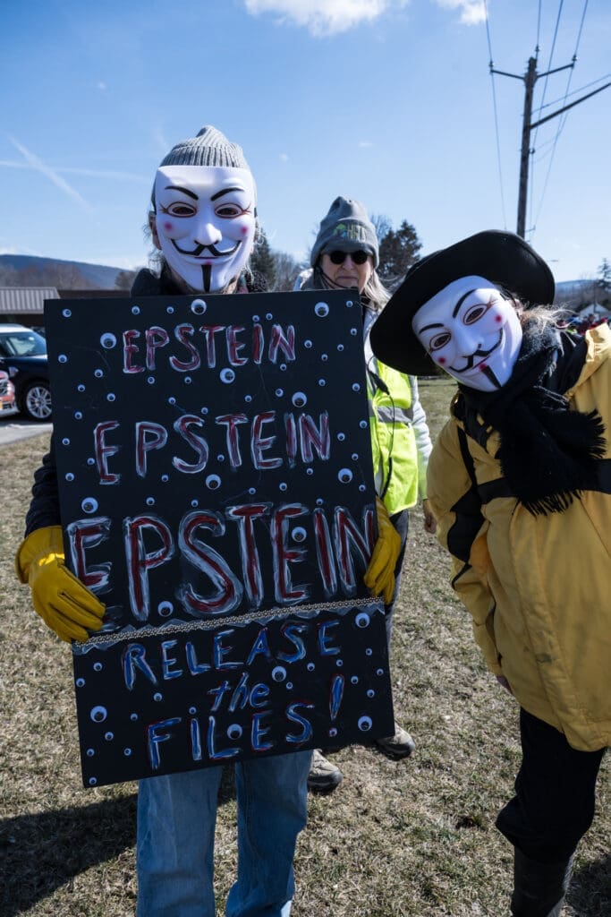 Protesters in Guy Fawkes masks holding Epstein sign