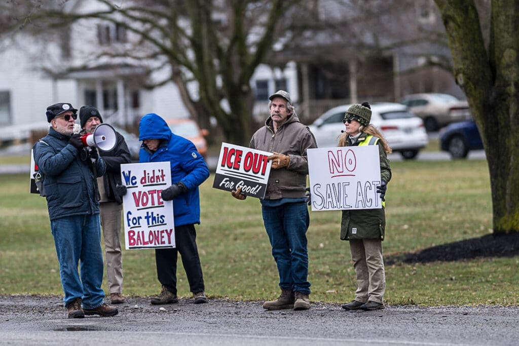 Protesters holding anti-ICE and SAVE Act signs.
