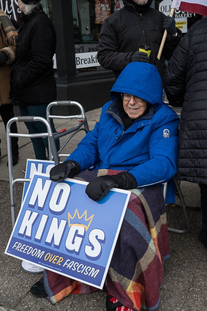 Elderly protester holding No Kings sign outdoors