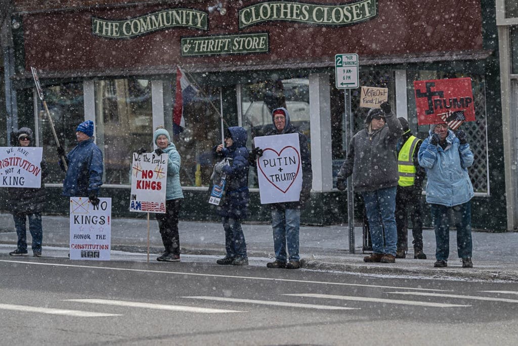 Protesters holding anti-Trump signs in snowy street.