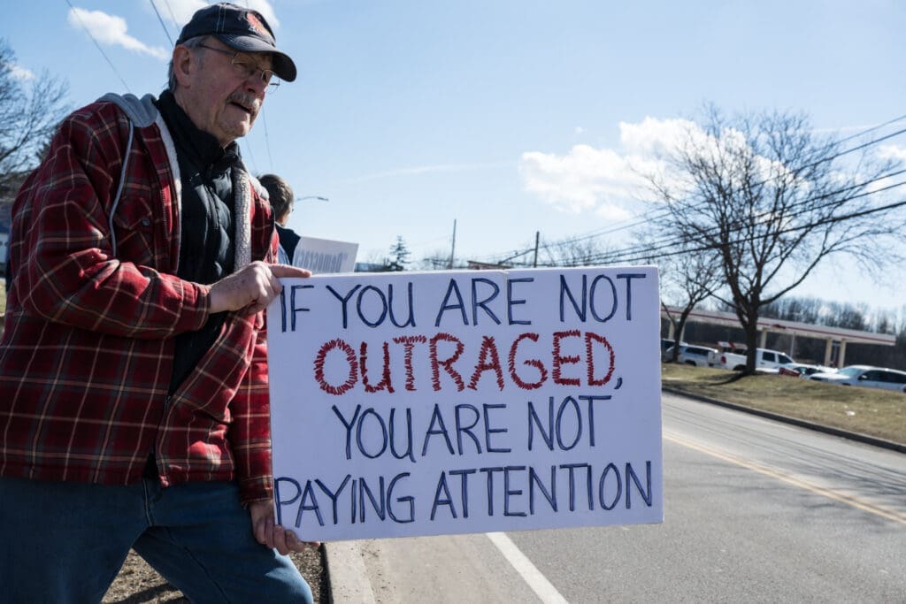 Elderly man holding protest sign about outrage and attention