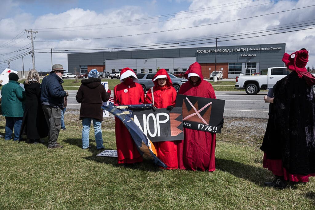 Protesters in red robes holding signs outside hospital