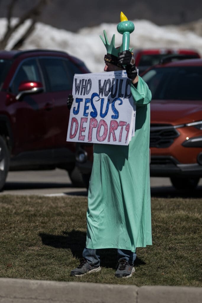 Person in Statue of Liberty costume holding protest sign