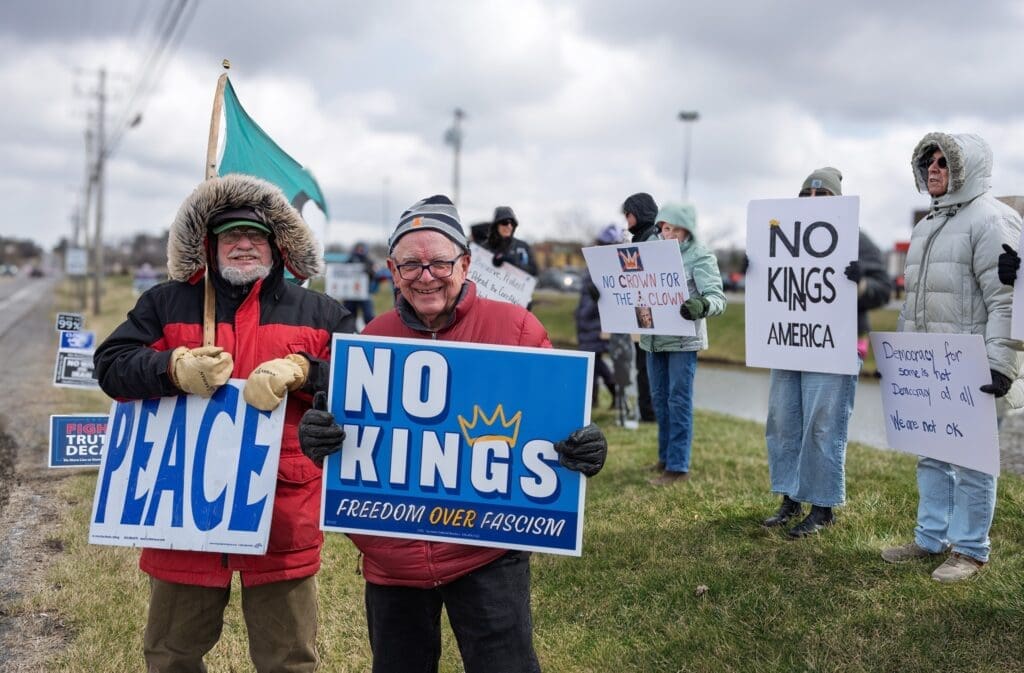 Protesters holding 'No Kings' and peace signs outdoors