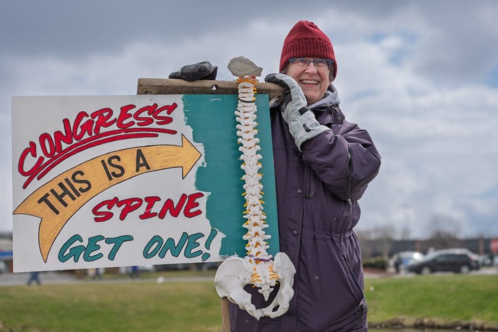 Woman holding Congress spine protest sign outdoors