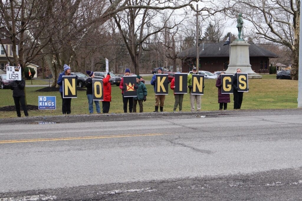 Protesters holding 'NO KINGS' signs roadside