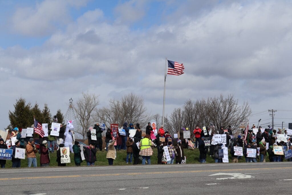 Protesters holding signs beneath American flag roadside