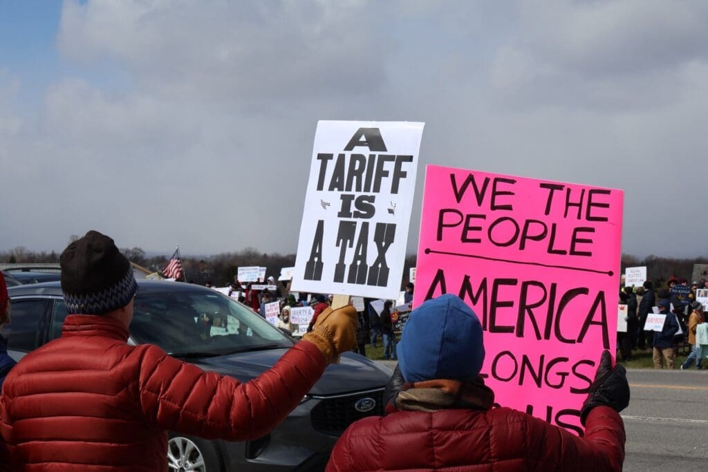 Protesters holding tariff and America signs roadside rally