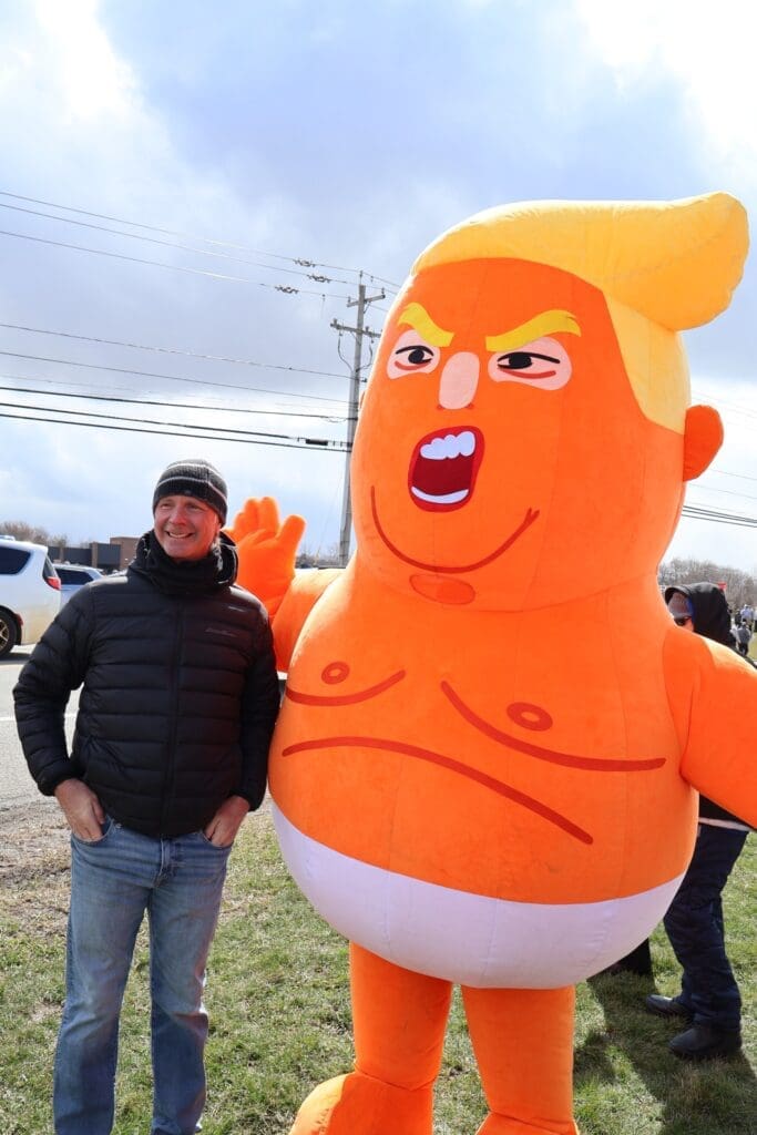 Man posing beside large orange inflatable caricature balloon