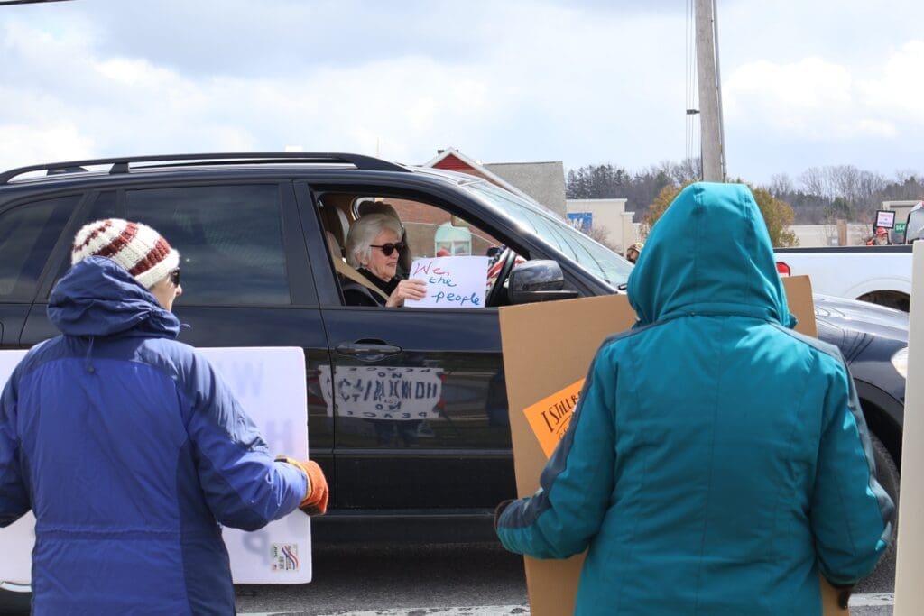 Woman in SUV holding protest sign to crowd