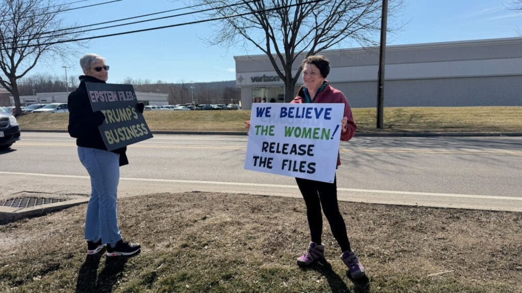 Two women holding protest signs supporting Epstein victims
