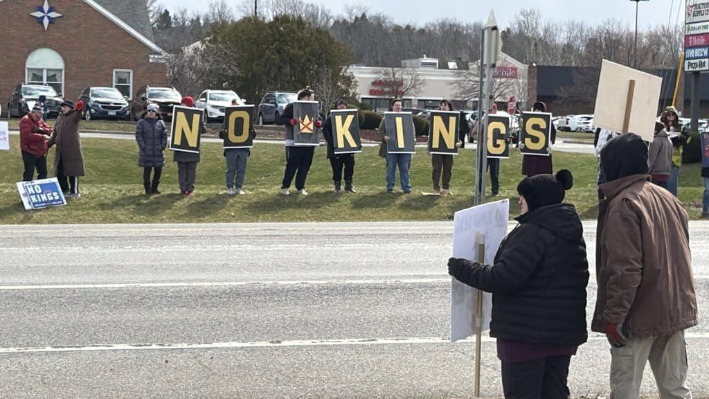 Protesters holding 'NO KINGS' signs along roadside