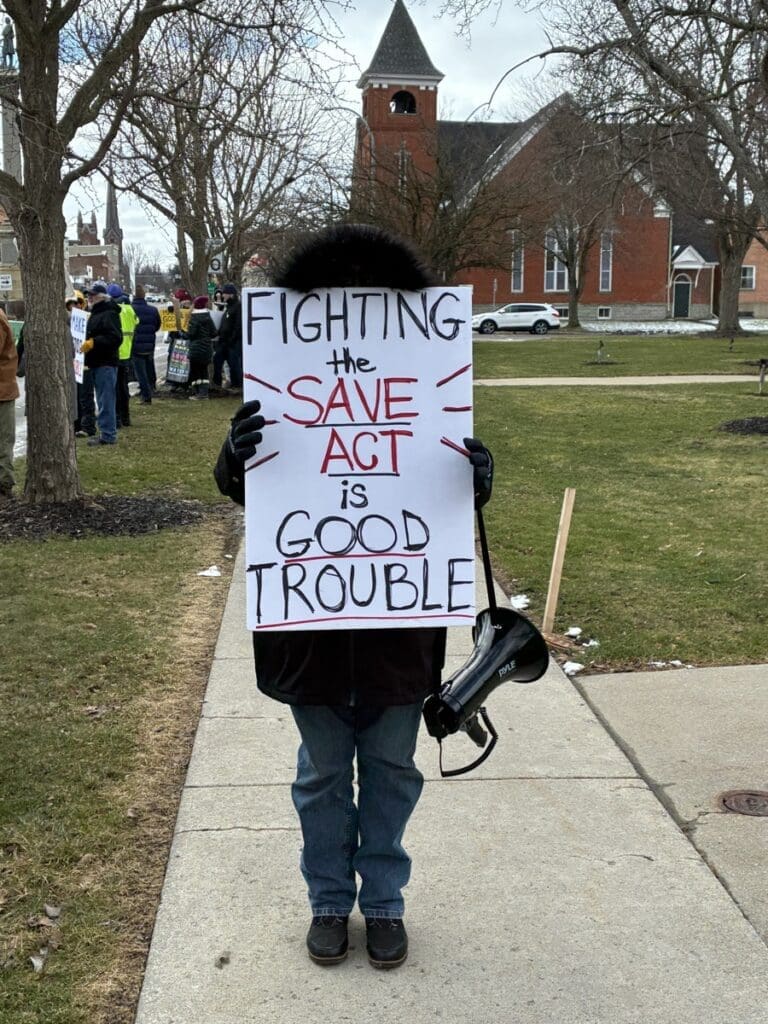Protester holding SAVE Act sign with megaphone
