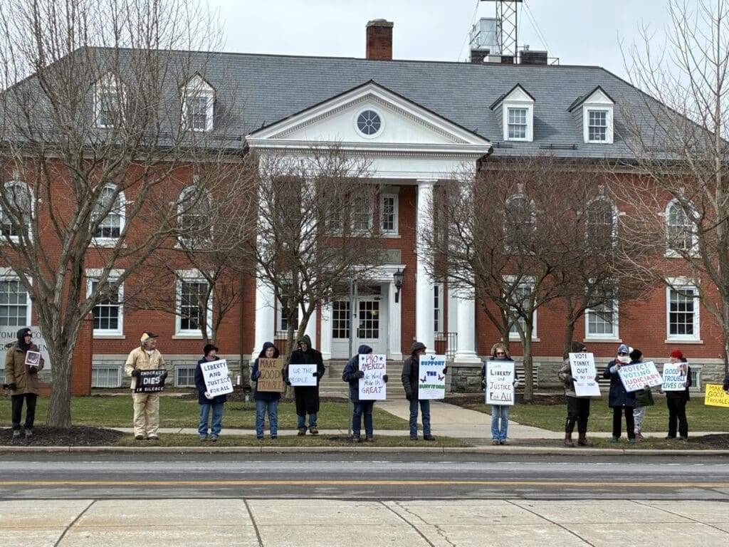 Protesters holding signs outside red-brick civic building