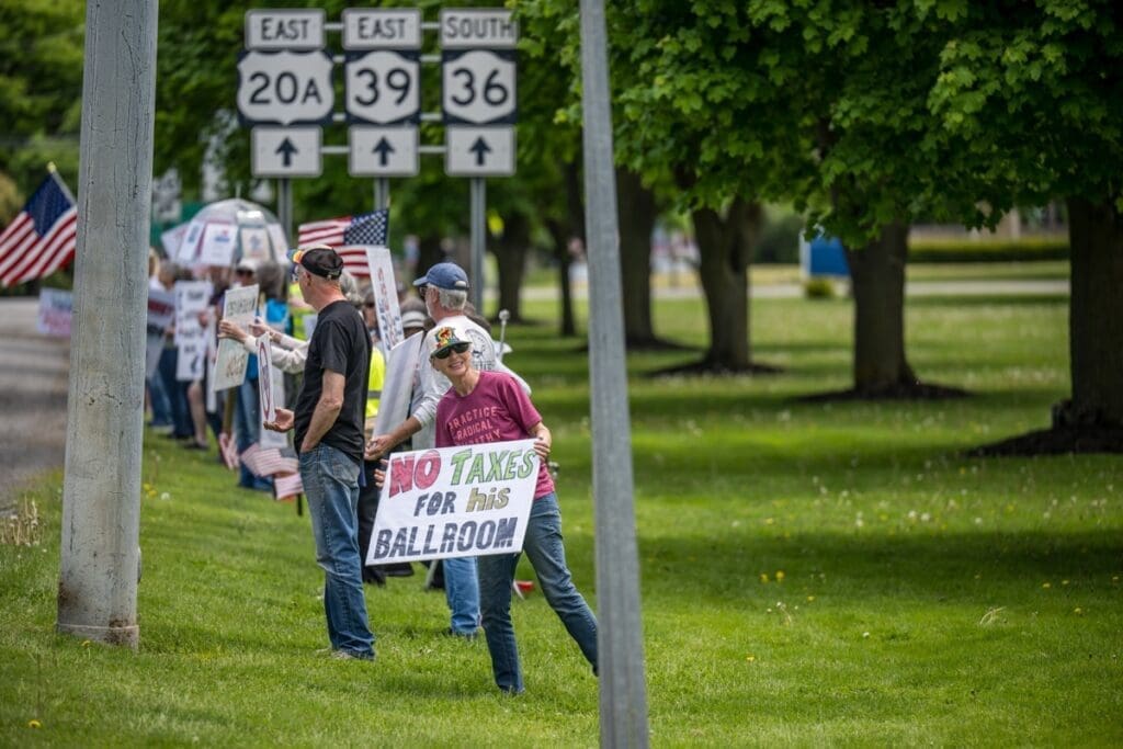 Protesters holding signs and flags by roadside intersection