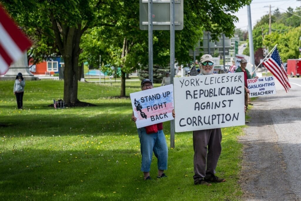 Protesters holding anti-corruption signs and American flags roadside