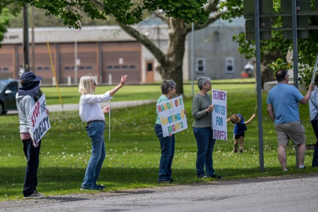 Protesters holding voting rights signs along roadside.