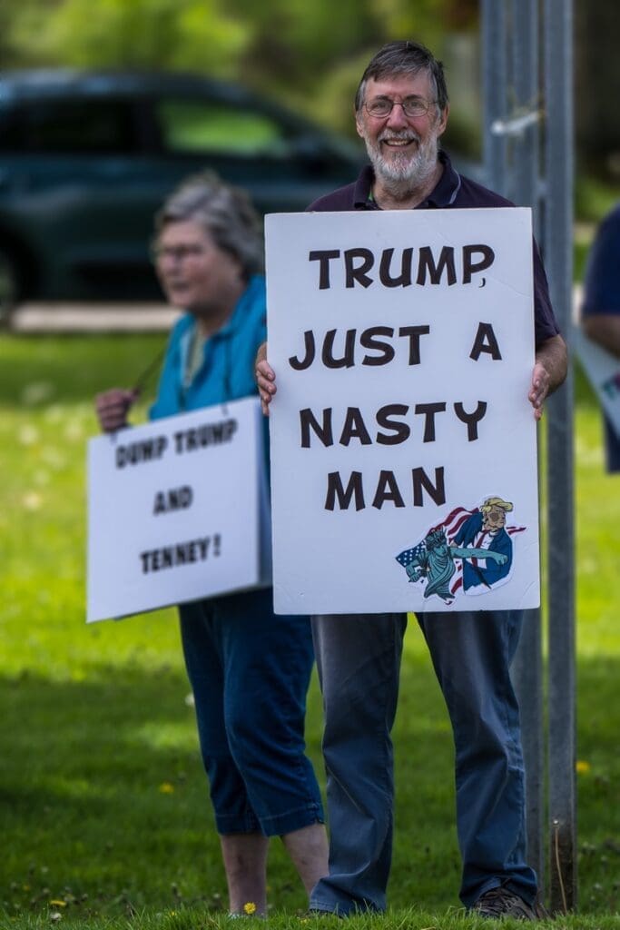 Man holding anti-Trump protest sign outdoors.