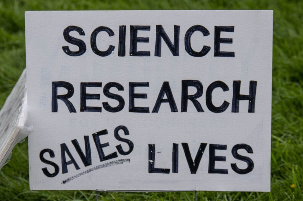 A yard sign boldly declares, "Science Research Saves Lives," set against a grassy backdrop. A simple yet powerful message advocating for the importance of scientific discovery.