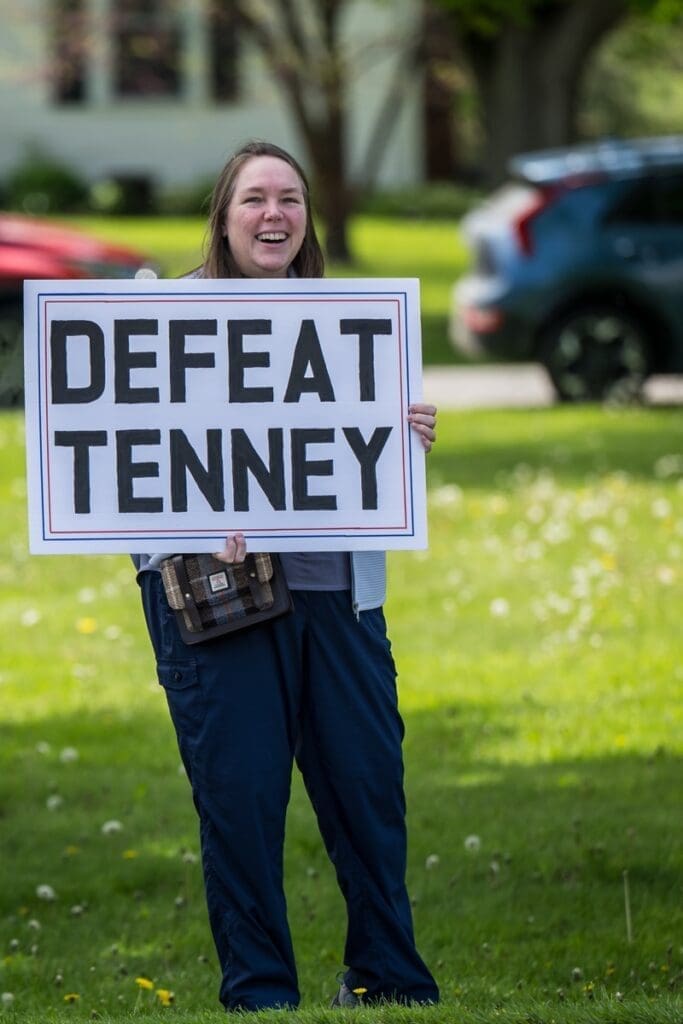 Woman holding 'Defeat Tenney' protest sign outdoors