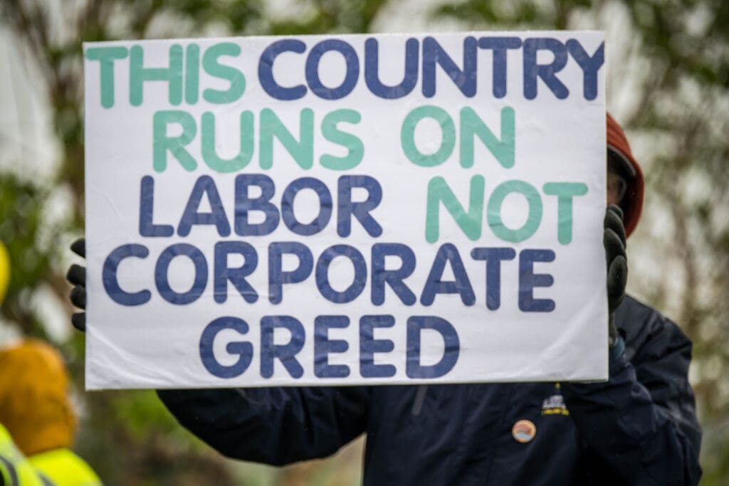 A protester holds a bold sign declaring, "This country runs on labor, not corporate greed." The message highlights a call for workers’ rights and economic fairness.