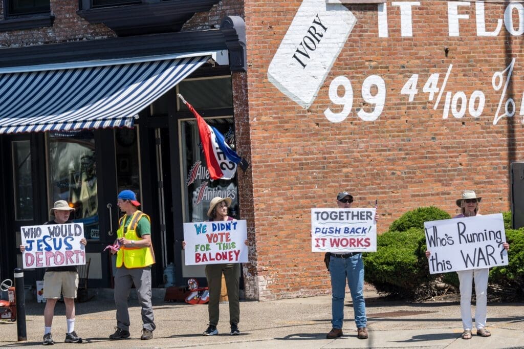 Protesters holding political signs on a city sidewalk