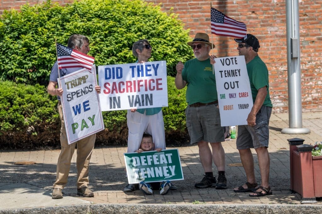 Protesters holding anti-Trump and Defeat Tenney signs outdoors