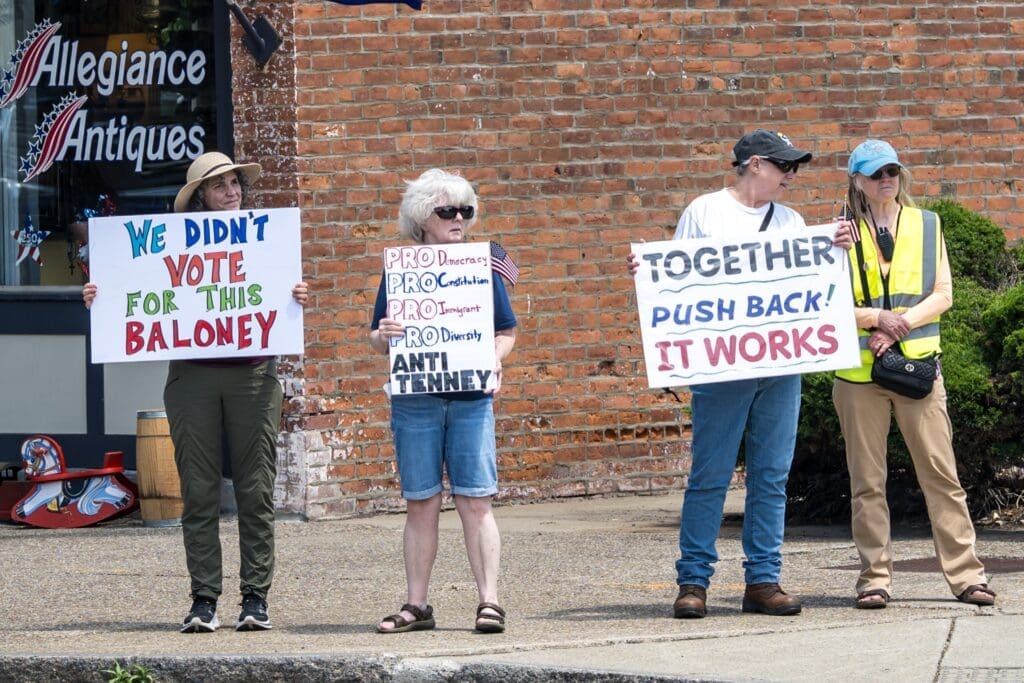 Four protesters holding political signs on a sidewalk