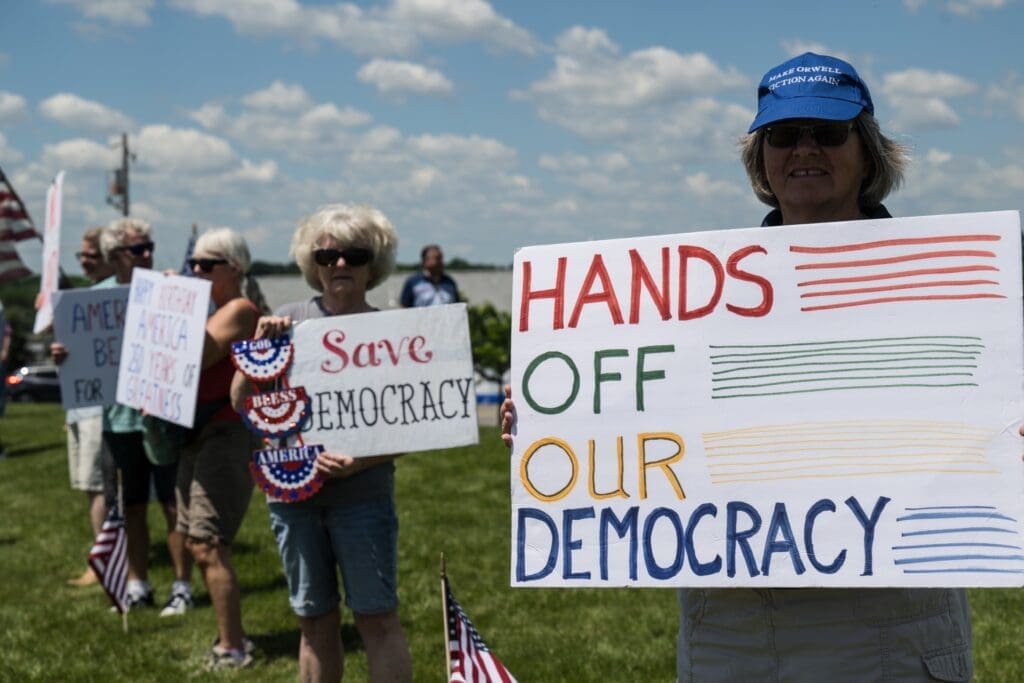 Protesters holding signs saying Hands Off Our Democracy outdoors