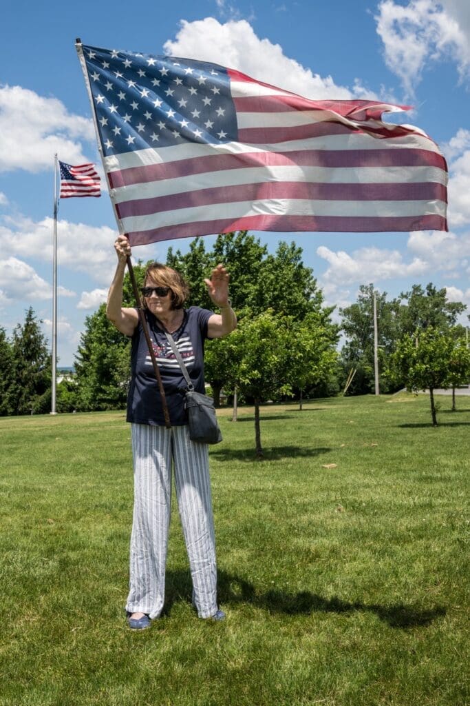 Woman proudly waving large American flag outdoors on sunny day