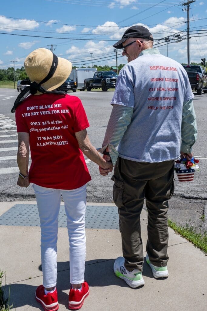 Elderly couple holding hands wearing political message shirts outdoors