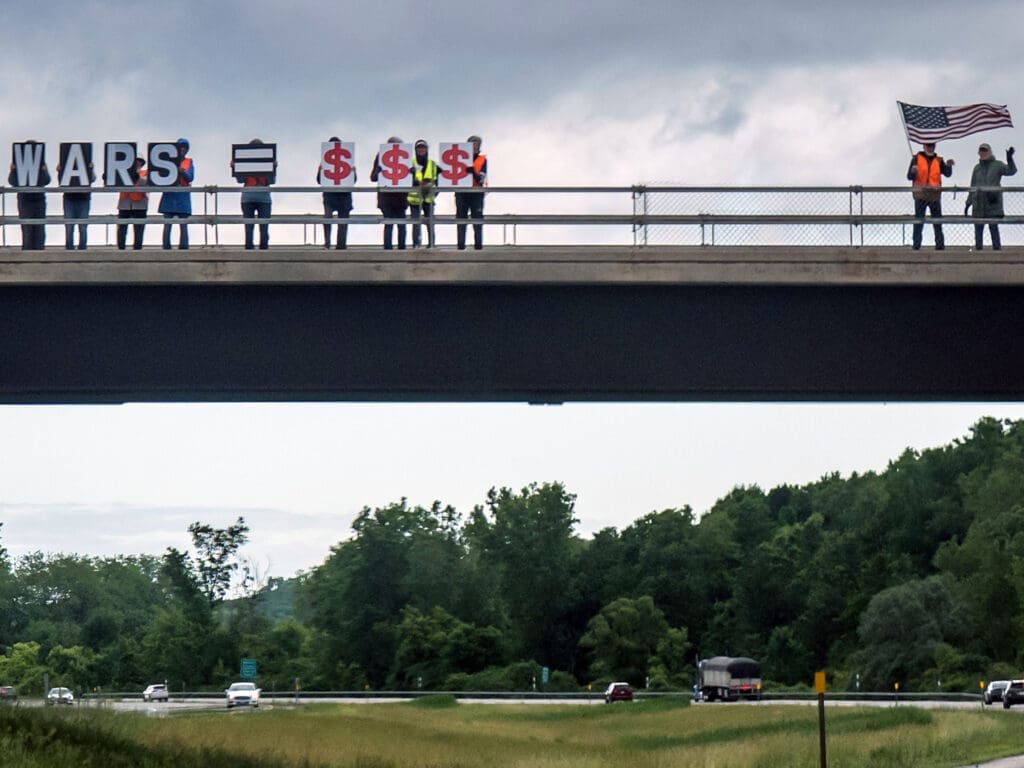 Protesters on highway overpass holding Wars equals money signs