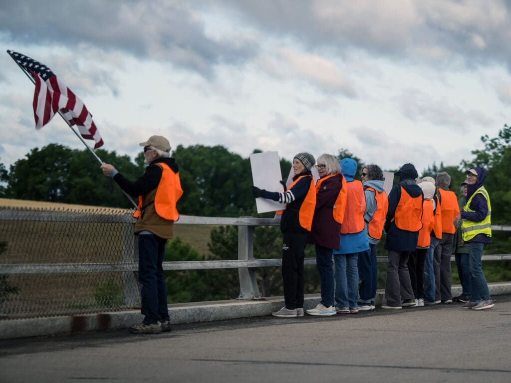 Group in orange vests waving American flag on bridge protest