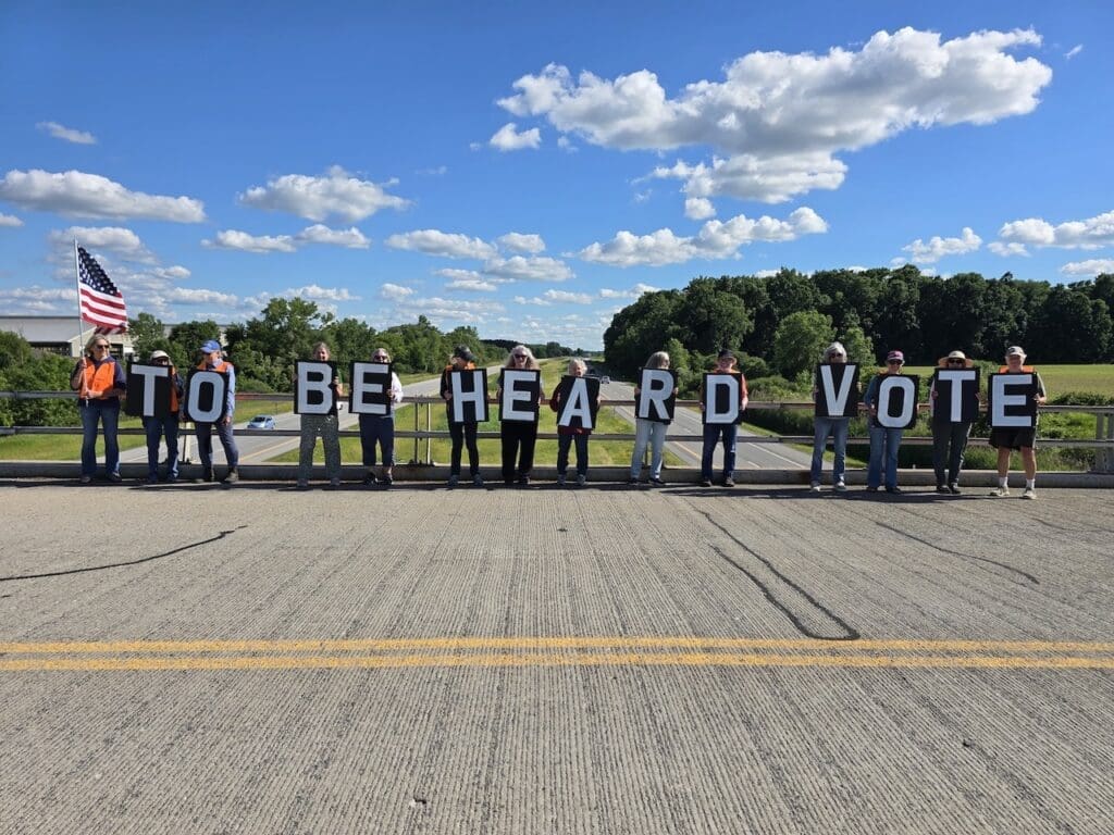 Group holding signs spelling 'To Be Heard Vote' on bridge