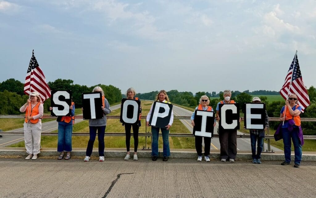 Protesters holding Stop ICE signs on highway overpass